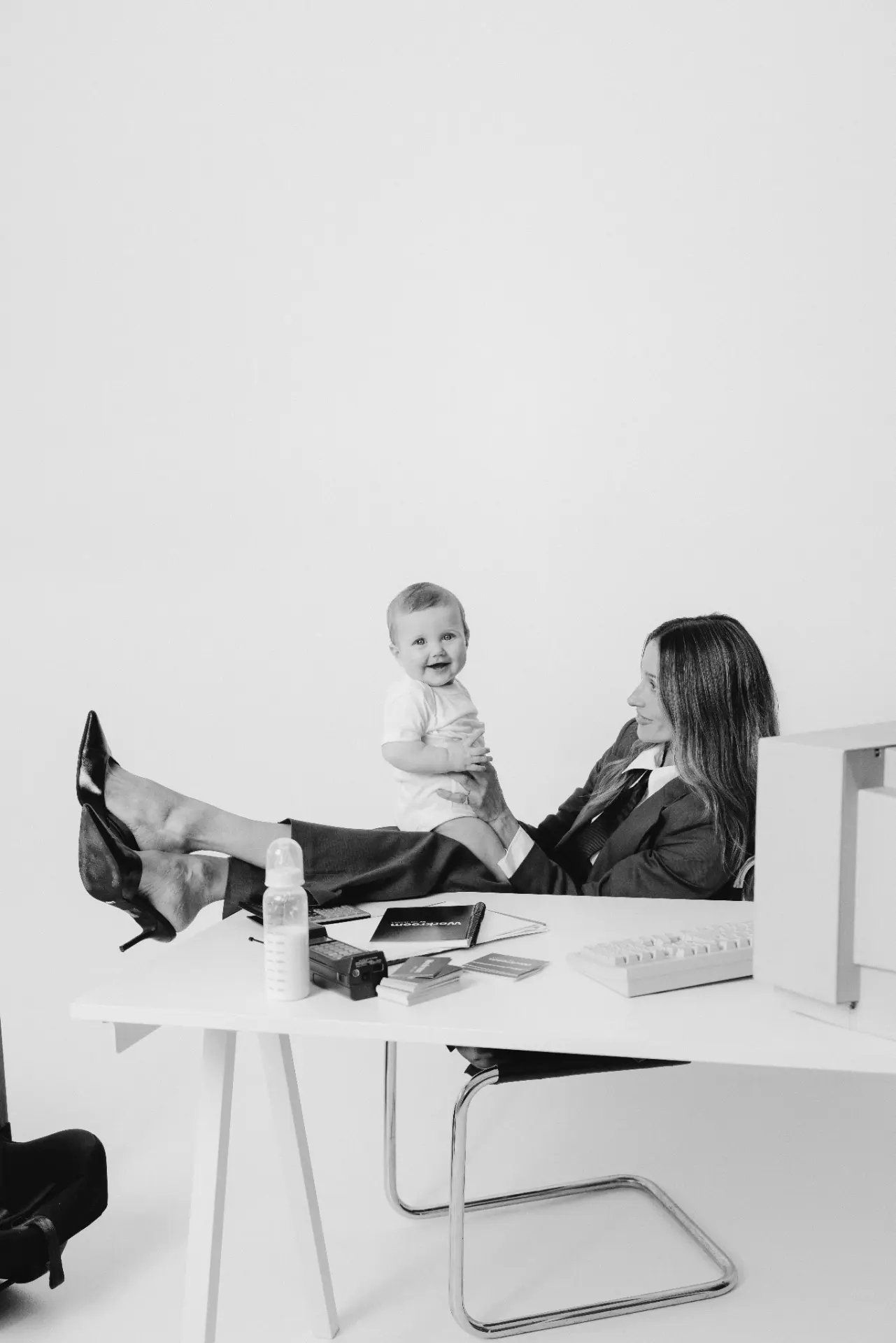 A mother at her desk, feet up, holding her smiling baby